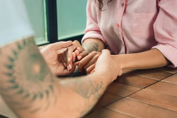 Cerca de un hombre y una mujer tomados de la mano en una mesa de madera — Foto de Stock