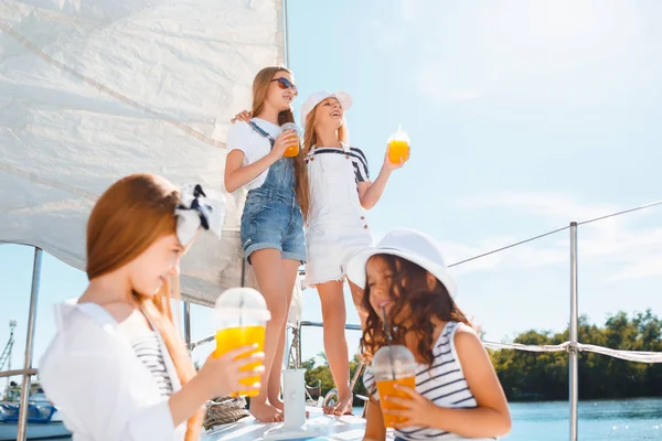海のボード上の子供はヨット飲むオレンジ ジュースです 青空屋外 代や子供の女の子 カラフルな服 子供ファッション 日当たりの良い夏 川と概念の休日 — ストック写真