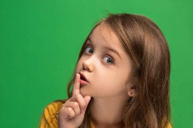 Yeşil arka plan üzerinde elini arkasındaki sır fısıldayan genç Genç kız