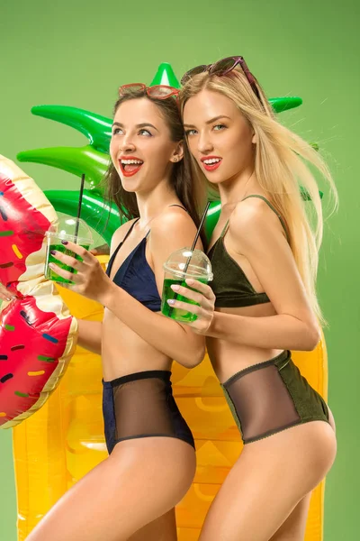 Cute girls in swimsuits posing at studio. Summer portrait caucasian teenagers on green background.
