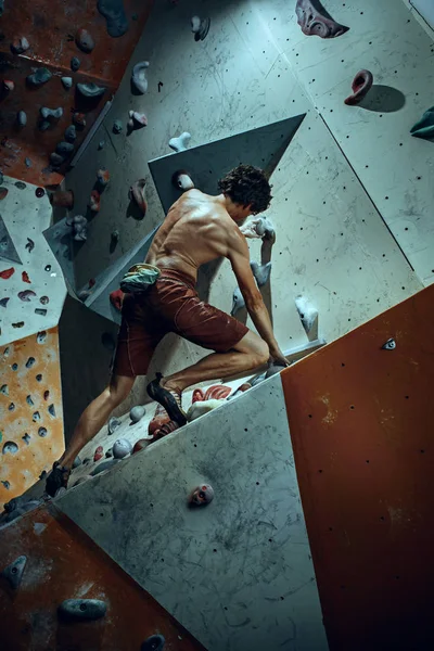 Jovem alpinista livre escalando pedregulho artificial dentro de casa — Fotografia de Stock