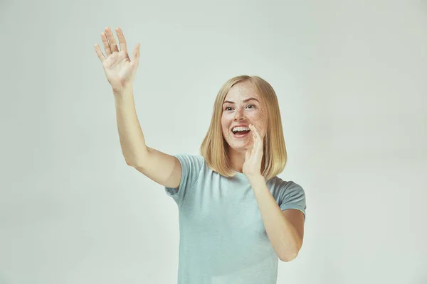 De gelukkige sproeterig vrouw permanent en glimlachend tegen de grijze achtergrond. — Stockfoto