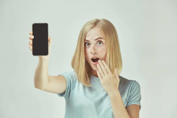 Retrato de una chica casual confiada que muestra el teléfono móvil en blanco aislado sobre fondo gris — Foto de Stock