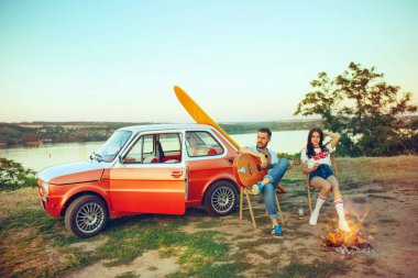 Çift oturma ve sahilde Nehri yakınında bir yaz gününde gitar çalmak dinlenme