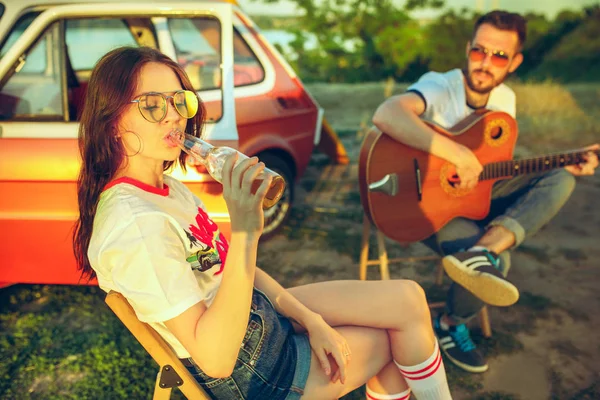 Coppia seduta e riposante sulla spiaggia a suonare la chitarra in una giornata estiva vicino al fiume — Foto Stock