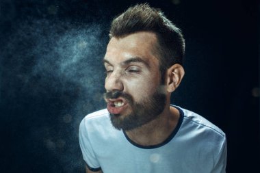 Sakal ve bıyık sprey ile sneezing ve küçük genç komik yakışıklı adam, stüdyo portre siyah arka plan üzerine damla. Komik, karikatür, mizah. hastalık, enfeksiyon, ağrı. Sağlık kavramı