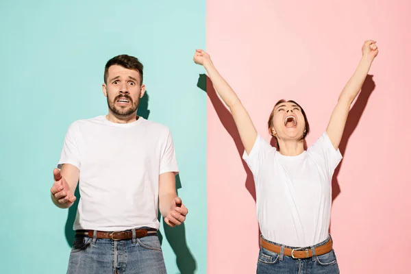 Retrato de primer plano de pareja joven, hombre, mujer. Uno emocionado feliz sonriente, otro serio, preocupado, infeliz sobre fondo rosa y azul. Contrastes de emoción — Foto de Stock