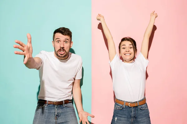 Retrato de primer plano de pareja joven, hombre, mujer. Uno emocionado feliz sonriente, otro serio, preocupado, infeliz sobre fondo rosa y azul. Contrastes de emoción — Foto de Stock