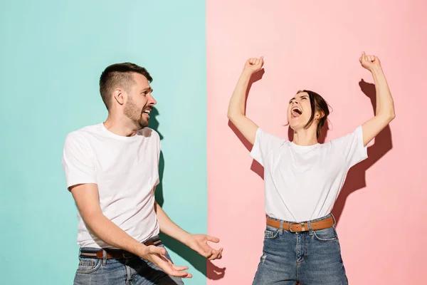 Closeup portrait of young couple, man, woman. One being excited happy smiling, other serious, concerned, unhappy on pink and blue background. Emotion contrasts — Stock Photo, Image