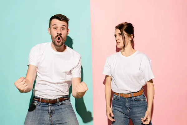 Retrato de perto de um jovem casal, homem, mulher. Um sendo animado sorrindo feliz, outro sério, preocupado, infeliz em fundo rosa e azul. Contrastes de emoção — Fotografia de Stock