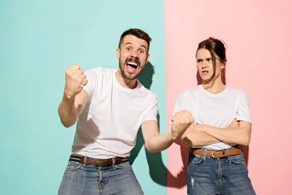 Closeup portrait of young couple, man, woman. One being excited happy smiling, other serious, concerned, unhappy on pink and blue background. Emotion contrasts — Stock Photo, Image