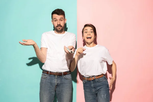 Closeup portrait of young couple, man, woman. One being excited happy smiling, other serious, concerned, unhappy on pink and blue background. Emotion contrasts — Stock Photo, Image