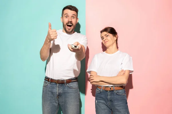 Closeup portrait of young couple, man, woman. One being excited happy smiling, other serious, concerned, unhappy on pink and blue background. Emotion contrasts — Stock Photo, Image