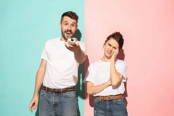 Closeup portrait of young couple, man, woman. One being excited happy smiling, other serious, concerned, unhappy on pink and blue background. Emotion contrasts — Stock Photo, Image