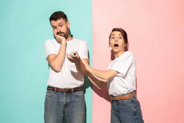 Closeup portrait of young couple, man, woman. One being excited happy smiling, other serious, concerned, unhappy on pink and blue background. Emotion contrasts — Stock Photo, Image
