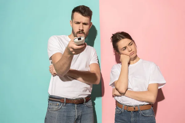 Casal entediado assistindo tv com a mão segurando o controle remoto de pé no estúdio — Fotografia de Stock