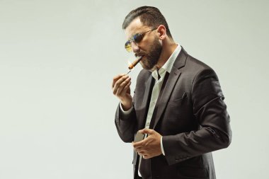 Puro tutan elbiseli barded adam. Gri studio arka plan üzerinde şık iş adamı. Güzel erkek portre. Duygusal delikanlı. İnsan duyguları, yüz ifadesi kavramı. İtalyan bak