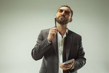 Erkek güzellik kavramı. Gri arka plan üzerinde poz trendy elbise giymiş şık saç kesimi ile şık genç bir adam portresi.