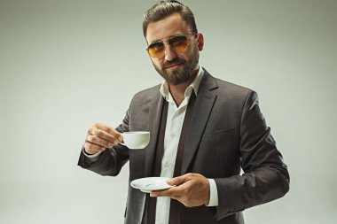 Erkek güzellik kavramı. Gri arka plan üzerinde poz trendy elbise giymiş şık saç kesimi ile şık genç bir adam portresi.