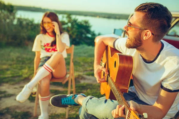 Par sitter och vilar på stranden spelar gitarr på en sommardag nära floden — Stockfoto