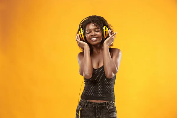 Retrato de estudio de adorable chica rizada feliz sonriendo durante la sesión de fotos. Impresionante mujer africana con piel marrón claro relajante en los auriculares —  Fotos de Stock