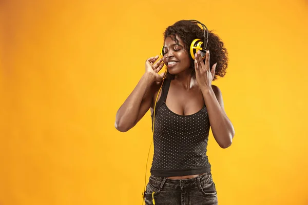 Retrato de estudio de adorable chica rizada feliz sonriendo durante la sesión de fotos. Impresionante mujer africana con piel marrón claro relajante en los auriculares —  Fotos de Stock