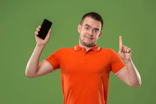 Den lyckliga mannen som visar på tomma skärmen på mobiltelefon mot grön bakgrund. — Stockfoto