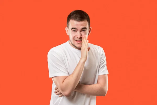 Der junge Mann flüstert ein Geheimnis hinter ihrer Hand vor orangefarbenem Hintergrund — Stockfoto