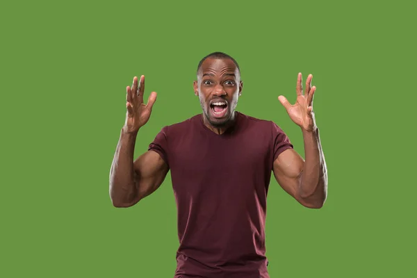 Молодой эмоциональный сердитый мужчина кричит на зеленом фоне студии — стоковое фото