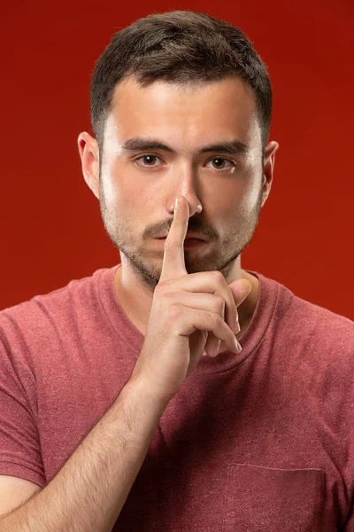 Der junge Mann flüstert ein Geheimnis hinter ihrer Hand vor rotem Hintergrund — Stockfoto