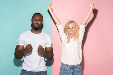 Biz kazandık. Kazanan başarı mutlu afro erkek ve kadın bir kazanan olmak kutluyor. Beyaz kadın ve erkek model pembe studio üzerinde dinamik görüntü.