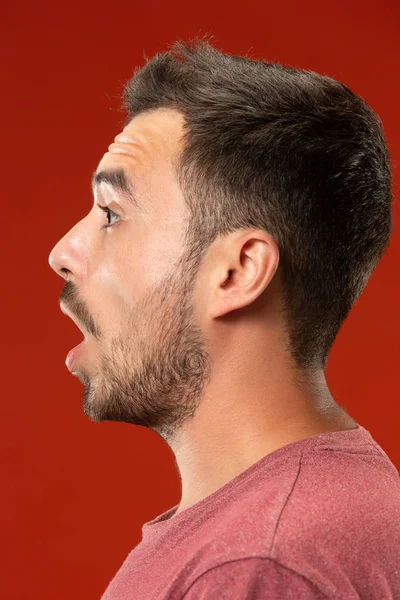 O jovem homem atraente olhando surpreendido isolado no vermelho — Fotografia de Stock