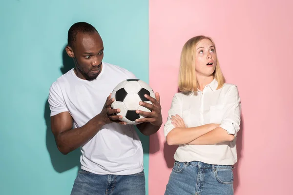Closeup portrait of young couple, man, woman with football ball. They are serious, concerned on pink and blue background. — Stock Photo, Image