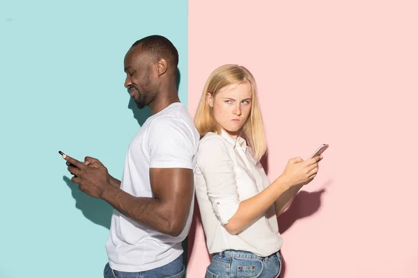 Смешанная гонка двух студентов, принимающих мобильные телефоны. Белая девушка и ее африканский парень позируют в студии  . — стоковое фото