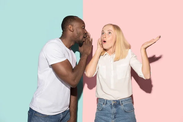 The young couple whispering a secret behind her hand over studio background — Stock Photo, Image