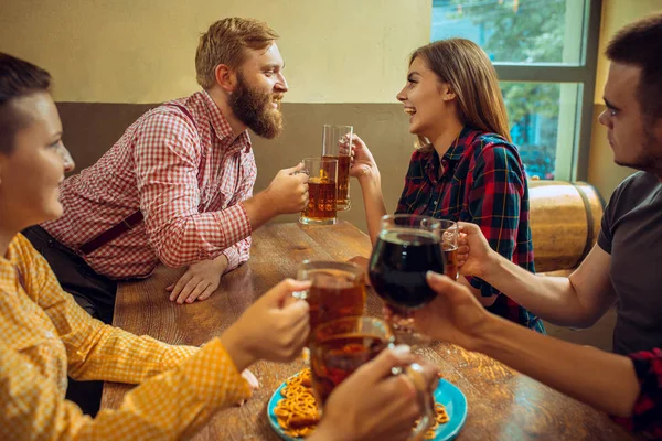 Personas, ocio, amistad y concepto de comunicación - amigos felices bebiendo cerveza, hablando y tintineo vasos en el bar o pub — Foto de Stock