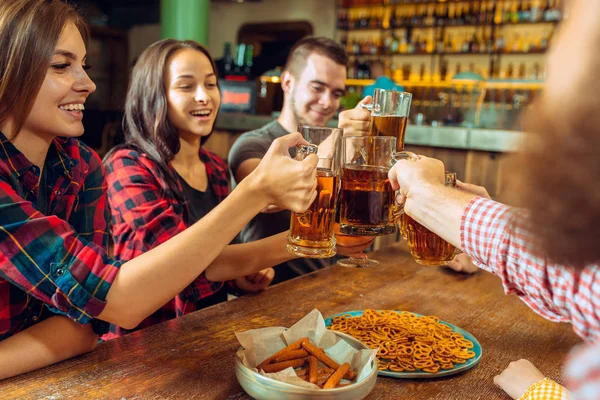 Personas, ocio, amistad y concepto de comunicación - amigos felices bebiendo cerveza, hablando y tintineo vasos en el bar o pub — Foto de Stock