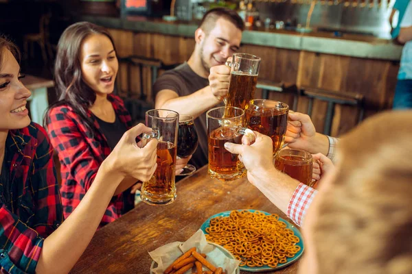 Concept de personnes, de loisirs, d'amitié et de communication - amis heureux buvant de la bière, parlant et cliquetant des verres au bar ou au pub — Photo