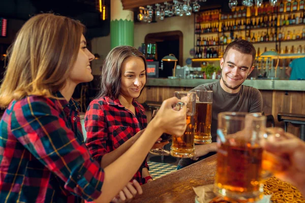 Concept de personnes, de loisirs, d'amitié et de communication - amis heureux buvant de la bière, parlant et cliquetant des verres au bar ou au pub — Photo