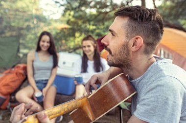 Parti, orman, kadın ve erkek grubunun kamp. Onlar, yeşil çim karşı bir şarkı söylerken rahatlatıcı. Tatil, yaz, macera, yaşam tarzı, piknik kavramı
