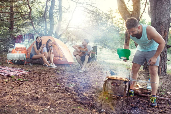 Fiesta, camping de hombres y mujeres grupo en el bosque. Se relajan, cantan una canción y cocinan barbacoa —  Fotos de Stock