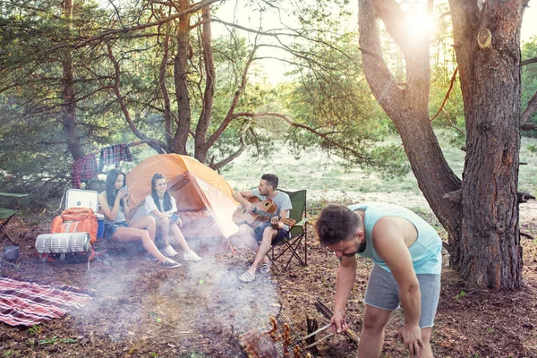 Вечеринка, кемпинг мужчин и женщин в лесу. Они отдыхают, поют песню и готовят барбекю — стоковое фото
