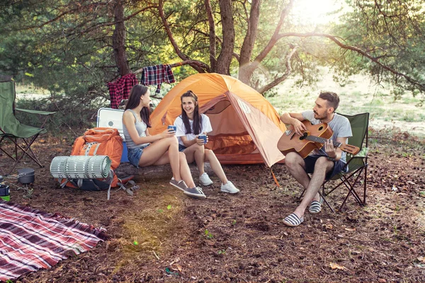 Fiesta, camping de hombres y mujeres grupo en el bosque. Se relajan, cantan una canción —  Fotos de Stock