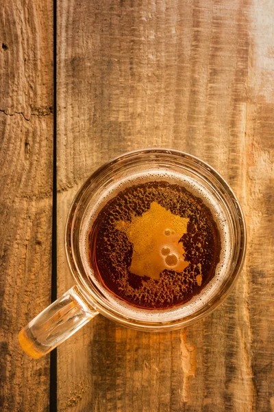 Conceito de cerveja francesa, silhueta da França em espuma em vidro de cerveja na mesa de madeira . — Fotografia de Stock