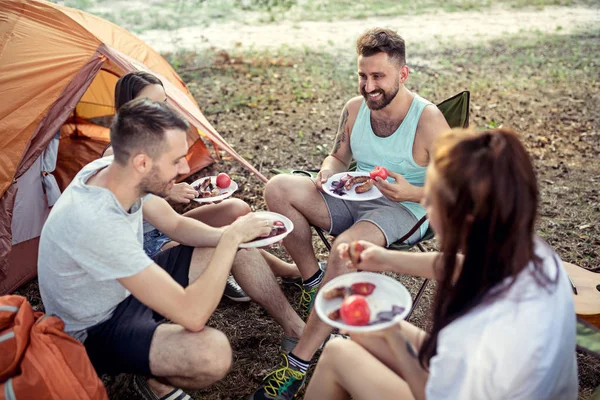 Fiesta, camping de hombres y mujeres grupo en el bosque. Ellos relajante y comer barbacoa —  Fotos de Stock
