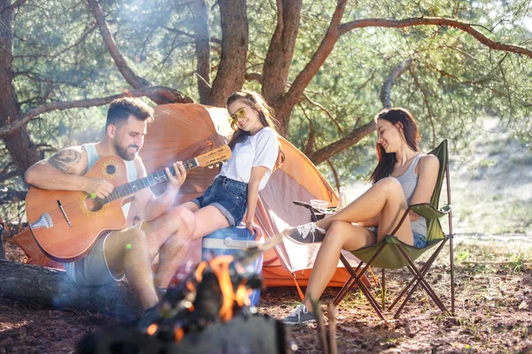 Impreza, camping grupy mężczyzn i kobiet, w lesie. One relaksujący, śpiewając piosenkę — Zdjęcie stockowe