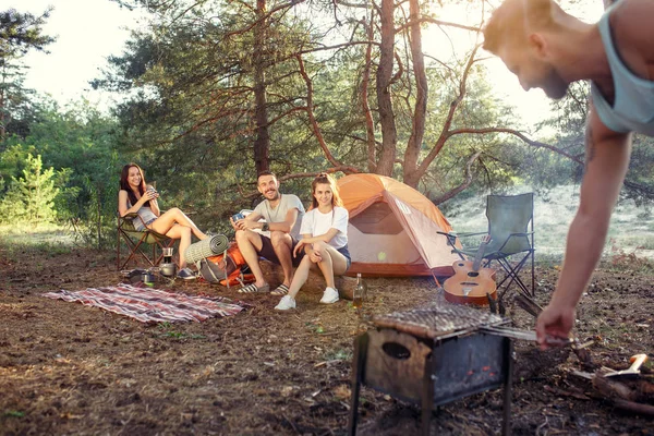 Party, camping of men and women group at forest. They relaxing, singing a song and cooking barbecue