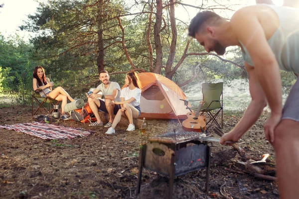 Strana, camping skupiny mužů a žen v lese. Relaxační, zpívá píseň a vaření grilování — Stock fotografie
