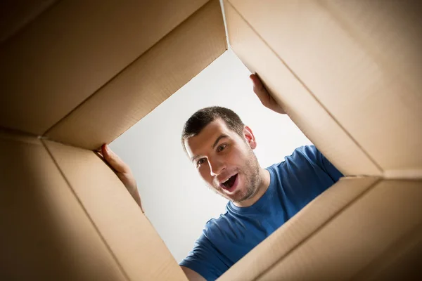 Чоловік розпаковує і відкриває картонну коробку і дивиться всередину — стокове фото