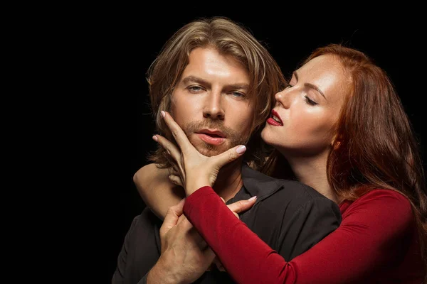 Real passion. Beautiful young loving couple bonding to each other while both standing against black studio walls